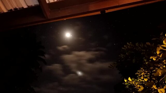 The moon caught on time lapse with clouds and stars moving across the sky from the terrace of a hawaiian home