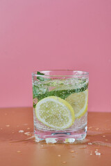 A glass of cold refreshing lemonade on pink background