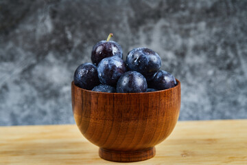 Garden plums in a bowl on wooden table