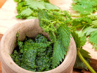 cooked and raw nettles on a wooden board and in a rustic mortar