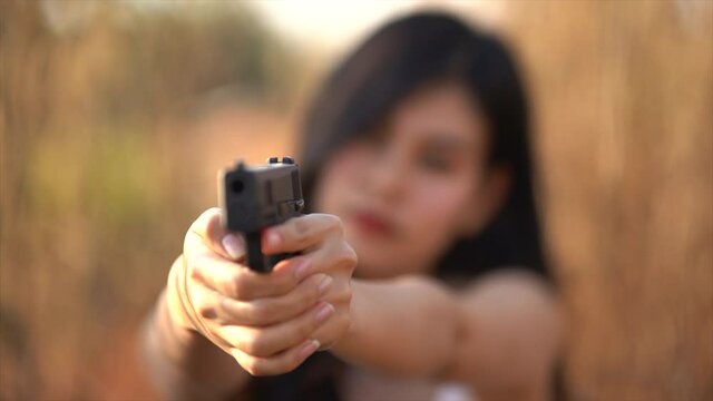 Beautiful asian women aim the gun on dry grass background