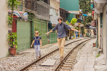Father and son travelers walk around railway paths which go through residential area in Hanoi city....