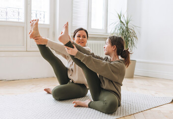 Attractive mother middle age woman and daughter teenager ptactice yoga together in the bright room