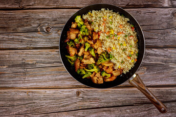 Stir-fry chicken and broccoli with rice in pan on wooden background.