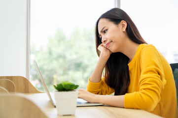 Asian young woman seriously working on computer laptop in house. She thinking find solution problem...