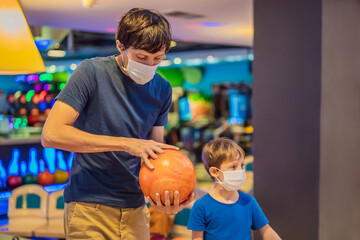 Fototapeta premium Father and son playing bowling with medical masks during COVID-19 coronavirus in bowling club