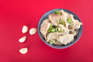 A bowl of dumplings and garlic on a red background