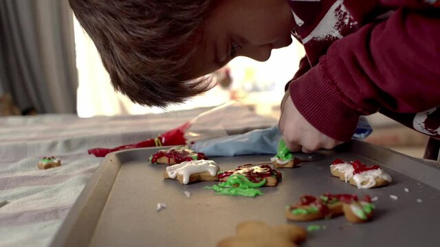 Close up shot of kid decorating homemade gingerbread cookies with coloured sugar icing at home. Side view 4k