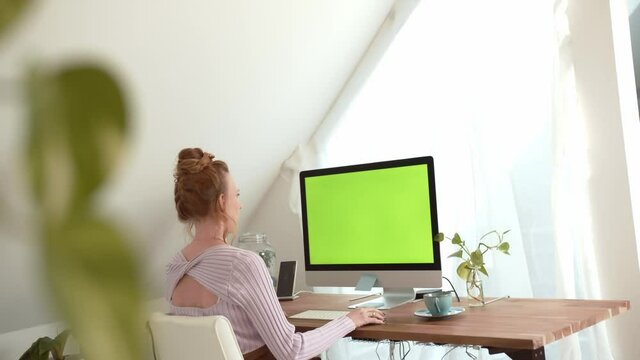 Woman is working in home office in front of a computer. Advertise Concept for Website, Application or Business. Young lady is sitting in front of a monitor with green screen chroma key.