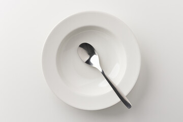 A white plate on a white table with a spoon There is no food on the plate. Household equipment