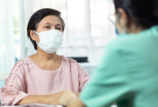 Asian Elderly woman patient wearing protective face mask talking consulting with Female Doctor or Nurse in medical office clinic or hospital