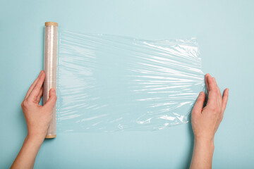 roll of plastic food film on blue background. Cling film in woman's hands. Woman's hand using a roll of transparent polyethylene food film for packing products on the blue table. body wrap - 408202035