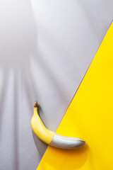 Banana painted silver color on a yellow and gray background. Minimalistic abstract food image