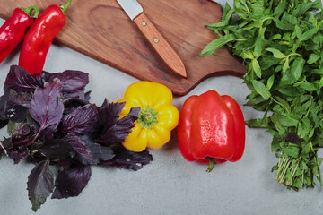 Fresh vegetables. Peppers, mint, basil on gray background with wooden board and knife