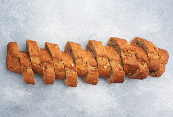 Sliced rye baguette on a gray background with cereals. Whole grain bread, a healthy food concept. Copy space.