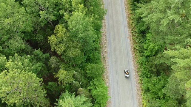Drone tracking shot going upwards of someone driving an ATV on a dirt road surrounded by green pine trees in Canada. 