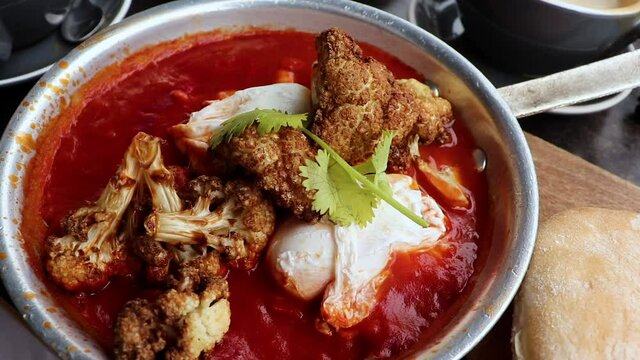 Slow motion shot of Shaksouka for breakfast. This is a very popular dish in North Africa and Shakshouka is a Maghrebi dish of eggs poached in a sauce of tomatoes, olive oil, peppers, onion and garlic.