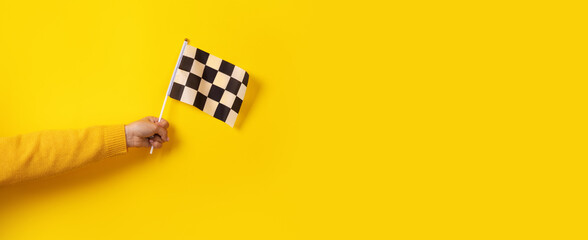 checkered flag in hand over yellow background, panoramic image - obrazy, fototapety, plakaty