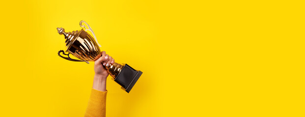woman holding up a gold trophy cup as a winner in a competition, panoramic image - obrazy, fototapety, plakaty