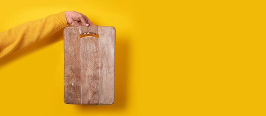 female hand holding wooden cutting board over yellow background