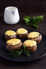Baked mushrooms stuffed with cheese and herbs on a black plate. wooden background.