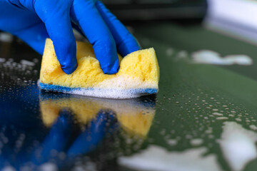 Men's hand in blue glove washes the modern electric hob with a sponge and cleansing foam. Close-up view