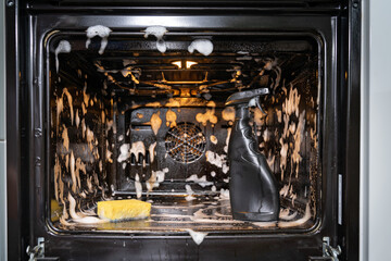 the spray bottle and sponge in the middle of the oven is covered with cleaning foam. home cleaning concept