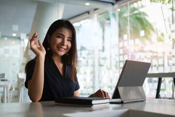 Portrait of happy young woman working on tablet pc while sitting at her working place in office.	