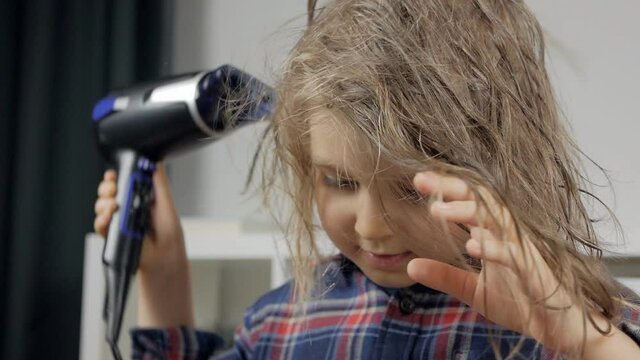 Little baby girl dries her hair with a hair dryer. Independent children. Hair care.