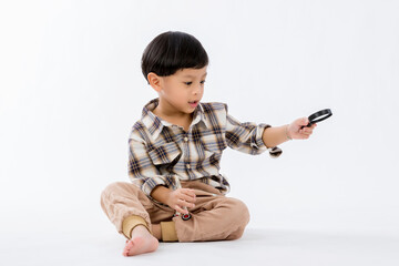 Child holding magnifying glass on white background. Boy with a magnifying glass in studio. Positive curious boy in casual wear looking at through magnifier 