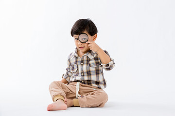 Child holding magnifying glass on white background. Boy with a magnifying glass in studio. Positive...