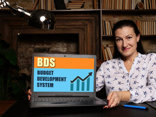 Woman showing laptop computer with  BDS BUDGET DEVELOPMENT SYSTEM icon on screen background,...