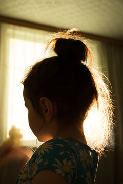 vertical banner of a little girl silhouette with her face in the dark and hair shining in backlight from a window