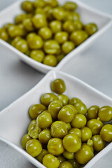 Two plates of boiled green peas on a grey background