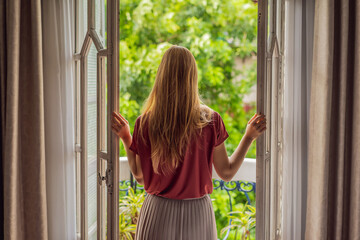 A ginger-haired woman stands on a heritage-style balcony enjoying her morning coffee. A woman in a hotel in Europe or Asia as tourism recovers from a pandemic. Tourism has recovered thanks to