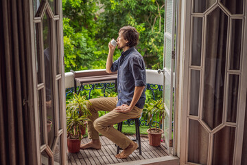 man stands on a heritage-style balcony enjoying his morning coffee. A man in a hotel in Europe or Asia as tourism recovers from a pandemic. Tourism has recovered thanks to vaccinations. Woman