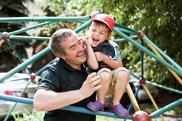 The father supports his son on the stairs on the Playground. Dad and son have fun together.
