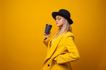 Take-away coffee. Stylish trendy young woman in bright clothes on a yellow background.