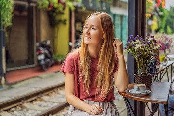 Young woman traveler drinks Vietnamese coffee with egg sitting by the railway paths which go through residential area in Hanoi city. Hanoi Train Street is a famous tourist destination. Vietnam reopens