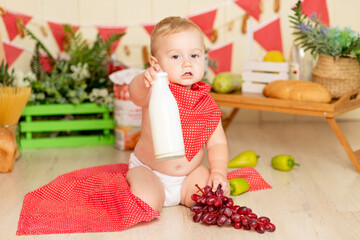 a small child a boy six months old is sitting on the kitchen floor with a bottle of milk and grapes