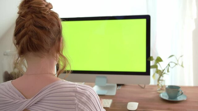Handsome Woman Sitting at her Desk using personal Computer with Green Screen. Chroma Key Mock-up for application, website, digital business and home office. Over Shoulder Shot filmed in 4K