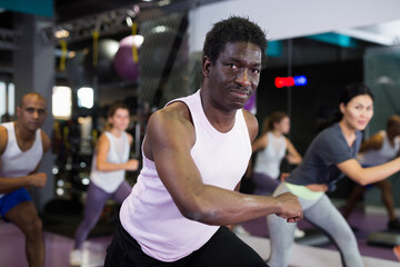 Fototapeta na wymiar African american man in group of sporty people working out with steppers in fitness center