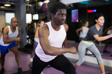 Fototapeta na wymiar African american man in group of sporty people working out with steppers in fitness center