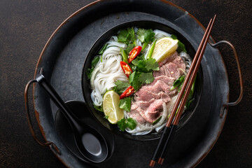 Pho Bo vietnamese soup with beef and rice noodles on a dark background, top view