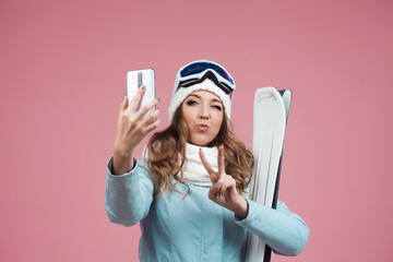 Fototapeta na wymiar fun skier takes a selfie on her smartphone. A young woman with ski equipment in a jacket and hat,