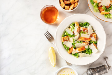 Caesar salad with the classic sauce and wine, overhead flat lay shot on a white marble background...