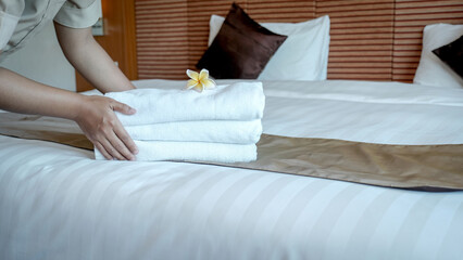 Hands of hotel maid putting plumeria flower and towels on the bed in the luxury hotel room ready...