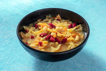 Vegan soup with vegetables, pasta and beans, on a blue background