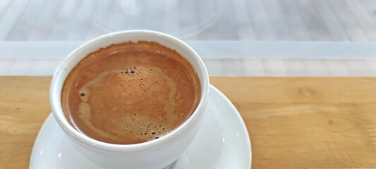 A hot coffee in white cup on wooden table.