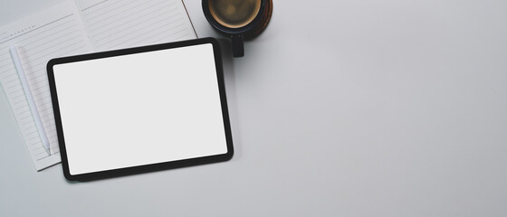Top view of mock up digital tablet, stylus pen, notebook, coffee cup  and copy space on white table.